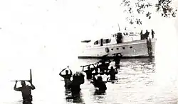 Cuban guerrillas holding rifles above their heads as they wade through the sea, having disembarked from a small boat