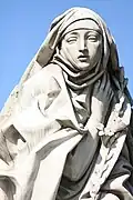St. Catherine of Siena, wearing a veil and mantle, holds a stalk of lilies.