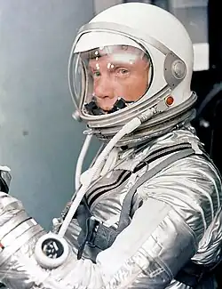 Glenn in a silver spacesuit, with his helmet on and clear visor down