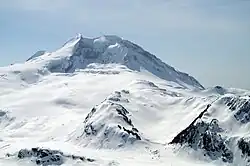 A snow-covered, cone-shaped mountain overlooking snow-covered and exposed slopes.