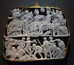 Sardonyx cameo with Augustus at top seated alongside Roman gods and being crowned with a laurel wreath. Below him a group of men lift a sigil standard.