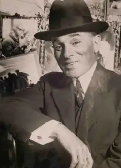 A sepia monochrome image featuring a man in a suit, tie and hat.
