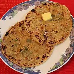 Two thick, brittle, round parathas with pieces of cauliflower and herbs