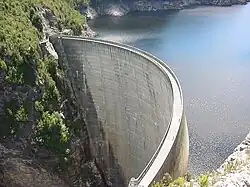 A thin, curved, concrete dam, impounding a large reservoir.
