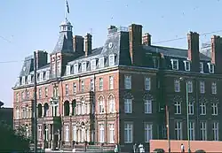 A grand red-brick hotel taken from its corner quite far way. It is designed a bit like a French chateau but with red brick and a slate roof.