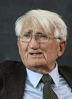 Photo of a man with white hair and glasses wearing a suit