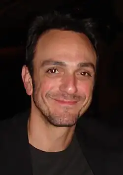 Head shot of broadly smiling man in black with receding dark hair and a day's beard growth on his face.