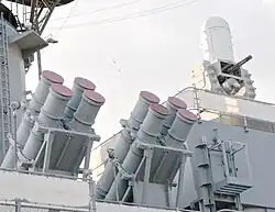 A quartet of grey colored cylindrical canisters positioned roughly in the center of the image, with the canisters pointed at angle with the base to the lower left. Another quartet is positioned on the left of the image. A white cylinder with a dome can be seen on the upper right of the image.