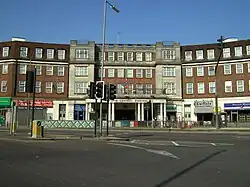 A brown-bricked building with white columns and a sign reading "HENDON CENTRAL STATION" in blue letters all under a clear, blue sky