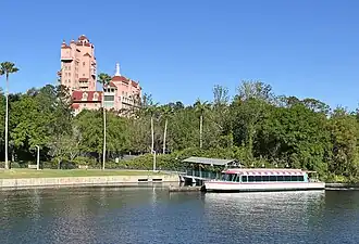 A water taxi is pictured docked at the entrance to Disney's Hollywood Studios. Behind the dock sits the exterior of the Twilight Zone Tower of Terror thrill ride. Due to its close proximity to EPCOT's Morocco pavilion, the back of the building, as pictured here, is specifically designed to hide the ride's horror theming and blend in with a Moroccan landscape.