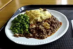 Photograph of a dinner plate on which a helping of minced lamb topped with mashed potato, served alongside peas.
