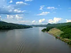A wide river with greenery on both sides and boats moving down it