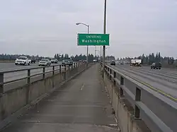 View of a narrow concrete pathway between freeway lanes, separated by a concrete barrier topped with metal railings