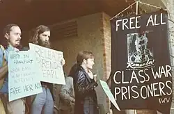 People holding signs near a banner demanding, "Free all class war prisoners!"