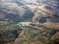 A rock dam is in a valley, with a reservoir behind it.