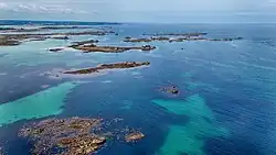 Aerial photograph showing shallow turquoise water and scattered rocky outcrops forming tidal flats near Roscoff in Brittany, France.
