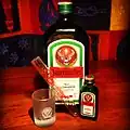 Jägermeister 700 ml bottle alongside a 20 ml bottle, a Jägermeister branded shot glass, and a Jägermeister branded test tube