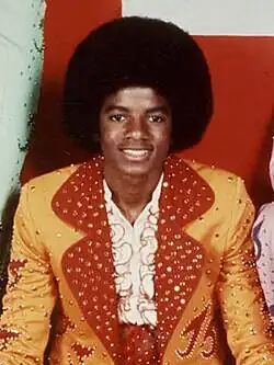 Jackson is wearing a yellow and red suit while sporting an afro for his haircut. His skin is dark