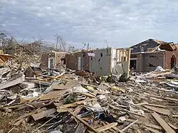 EF3 damage example-- The majority of the house was heavily damaged, with some trees uprooted in the background. Only a portion of a wall remains. Debris is scattered at the site of impact.