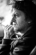 Black-and-white side-profile portrait of a seated person with messy hair, resting a hand on his chin