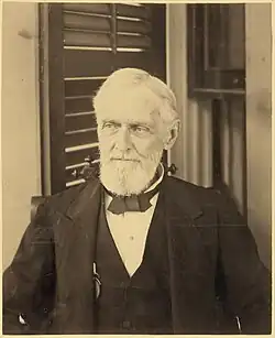 bearded man looking forward with shuttered window in background