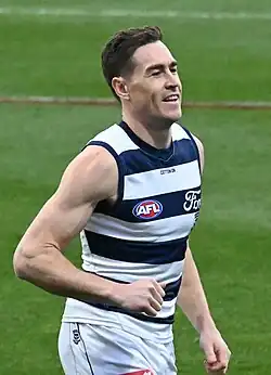 A man with short brown hair in a sleeveless yellow guernsey and black shorts