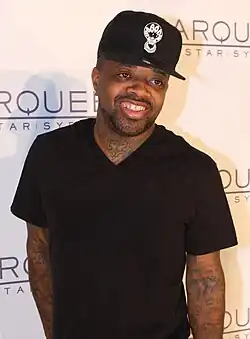 An African-American man wearing a black hat and shirt while smiling