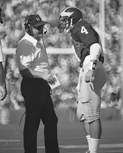 A black and white photo of two men standing. The man on the left is Bo Schembechler the coach of Michigan. On the right is Jim Harbaugh.