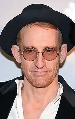 A close-up shot of a man with glasses wearing a black hat