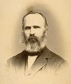Portrait of a middle-aged man with full beard and thinning hair is wearing a formal jacket.