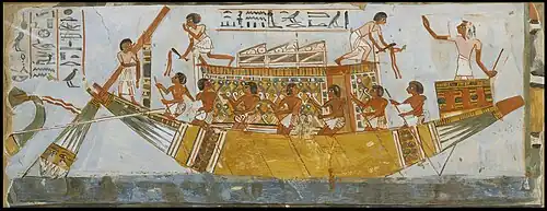 A painting on a wall of a boat on a river, with Ancient Egyptians rowing it