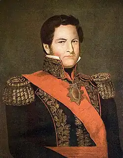 Half-length painted portrait of a man with curly hair, long sideburns and blue eyes who wears a heavily embroidered military tunic with high collar, gold braid epaulettes and a red sash of office