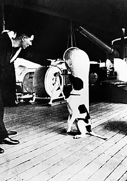 A dog sitting on the deck of a ship, being spoken to by a man in a military uniform