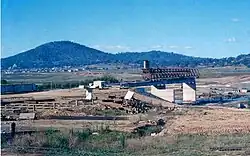 Kings Avenue Bridge under construction. The bridge is incomplete and only the pylons and platform on the southern side are in place. The site is surrounded by dust and the lakebed is dried out.