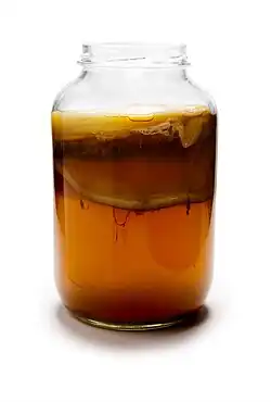Glass jar filled with brown kombucha beverage, including the floating culture