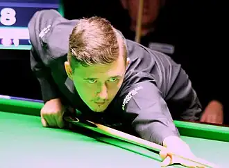 Photograph of Kyren Wilson leaning across the table, holding a cue.