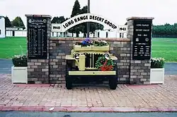 Front end of a jeep, sticking out of brick wall with plaques on brick pillars either side