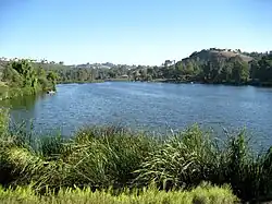 A light-blue reservoir formed by a large dam across a broad valley ringed by houses