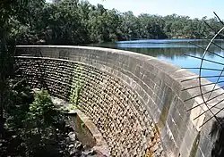 A stone dam with a reservoir behind it, surrounded by trees.