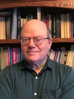 Headshot of a bespectacled balding man in a chequered shirt facing the camera.