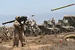 A large pipe-like weapon with a box on its lower right hand side and upper right hand side, shouldered by a U.S. Marine. The separated ejection motor and launched missile are visible to the right.