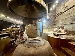 A restaurant kitchen where cooks are preparing lavash using an above-ground tandoor.