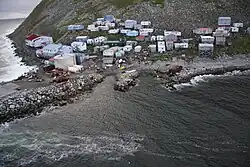 A village of 40–50 mostly small buildings built on a steep, rocky coastline; some structures higher on the hill are built on stilts