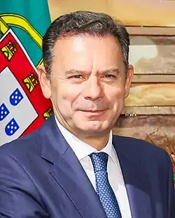 Luís Montenegro smiling besides a Portuguese flag.
