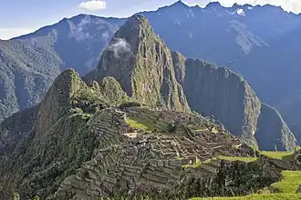 Stone ruins of Machu Picchu set on a mountain ridge, with steep green peaks in the background.