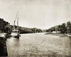 A photograph of a river, lined with trees on both banks, and a boat docked on the side.