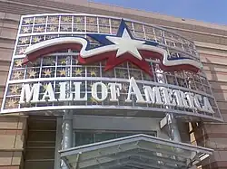 The logo for Mall of America themed after the United States flag. It is a white star with a blue outline with red and blue squiggly lines next to it. "MALL OF AMERICA" is underneath it.