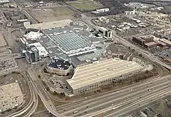 An aerial view of a square-shaped building (Mall of America) with a parking garage in front of it. Anchor stores are visible on its edges, with JW Marriott on the right. Several buildings and roads are in the background.