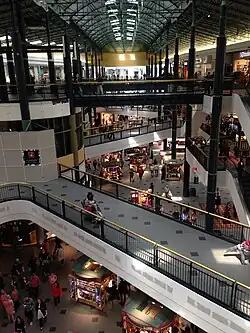 A three-level shopping mall corridor with a black paint job and golden railings. Kiosks are visible below.