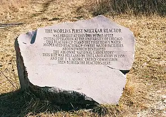 Image of the granite marker. The text reads: "The world's first nuclear reactor was rebuilt at this site in 1943 after initial operation at the University of Chicago. This reactor (CP-2) and the first heavy water moderated reactor (CP-3) where major facilities around which developed the Argonne National Laboratory. This site was released by the laboratory in 1956 and the U.S. Atomic Energy Commission then buried the reactors here."